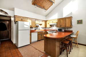 Kitchen featuring a kitchen bar, sink, high vaulted ceiling, kitchen peninsula, and white appliances