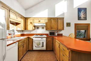 Kitchen with a high ceiling, sink, white appliances, and kitchen peninsula