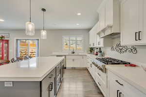 Kitchen featuring a center island, stainless steel gas cooktop, white cabinets, a kitchen bar, and decorative light fixtures