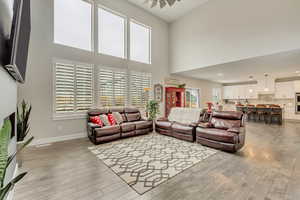 Living room with ceiling fan, a towering ceiling, and light wood-type flooring