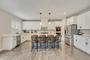 Kitchen with a kitchen island, appliances with stainless steel finishes, sink, white cabinets, and hanging light fixtures