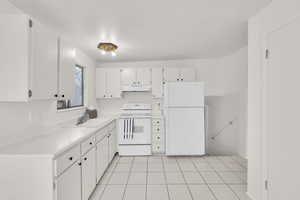 Kitchen featuring white cabinetry, sink, light tile patterned flooring, and white appliances