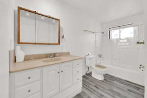 Full bathroom with vanity, hardwood / wood-style flooring, bath / shower combo with glass door, and toilet