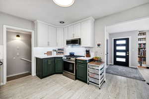 Kitchen with white cabinetry, green cabinetry, stainless steel appliances, light hardwood / wood-style floors, and backsplash