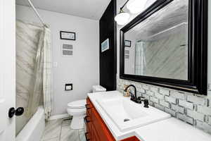 Full bathroom featuring tasteful backsplash, vanity, shower / bathtub combination with curtain, and toilet