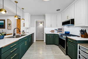 Kitchen featuring pendant lighting, sink, white cabinetry, stainless steel appliances, and green cabinetry