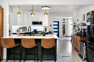 Kitchen with black fridge with ice dispenser, sink, white cabinetry, tasteful backsplash, and pendant lighting