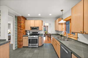 Kitchen featuring pendant lighting, sink, dark tile patterned floors, stainless steel appliances, and light brown cabinetry