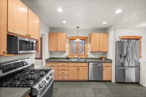 Kitchen featuring appliances with stainless steel finishes, decorative light fixtures, sink, and light brown cabinets