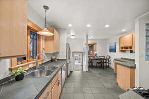 Kitchen featuring stainless steel appliances, decorative light fixtures, light brown cabinetry, and sink