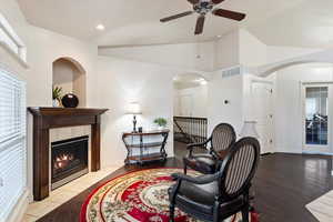 Living area featuring a tiled fireplace, lofted ceiling, dark hardwood / wood-style floors, and ceiling fan