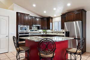 Kitchen featuring light tile patterned flooring, appliances with stainless steel finishes, sink, a center island, and light stone counters