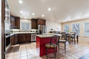 Interior space with a kitchen island, appliances with stainless steel finishes, lofted ceiling, dark brown cabinets, and light wood-type flooring