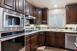 Kitchen with dark brown cabinetry, a breakfast bar area, light stone counters, a center island, and appliances with stainless steel finishes