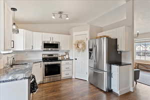 Kitchen featuring lofted ceiling, sink, white cabinetry, hanging light fixtures, and stainless steel appliances