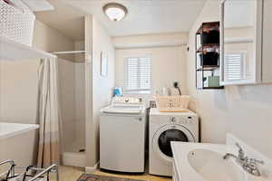 Clothes washing area with washing machine and clothes dryer, sink, and a textured ceiling