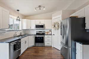 Kitchen with pendant lighting, lofted ceiling, sink, white cabinets, and stainless steel appliances