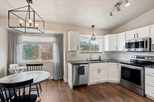 Kitchen featuring white cabinetry, sink, decorative light fixtures, and appliances with stainless steel finishes