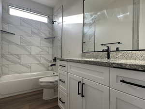 Full bathroom featuring tiled shower / bath, hardwood / wood-style floors, vanity, and toilet