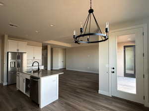 Kitchen featuring appliances with stainless steel finishes, sink, white cabinets, dark stone counters, and a kitchen island with sink