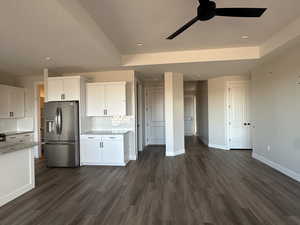 Kitchen featuring stainless steel refrigerator with ice dispenser, tasteful backsplash, light stone countertops, white cabinets, and dark hardwood / wood-style flooring