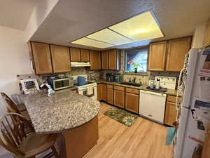 Kitchen featuring sink, white appliances, a kitchen breakfast bar, light hardwood / wood-style floors, and kitchen peninsula