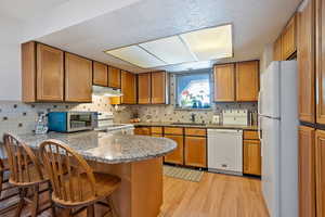 Kitchen featuring under cabinet range hood, a peninsula, white appliances, light wood-type flooring, and brown cabinets