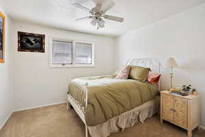 Bedroom featuring a ceiling fan, baseboards, a textured ceiling, and light colored carpet