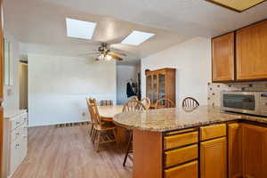 Kitchen with a peninsula, stainless steel microwave, light wood-type flooring, and brown cabinets