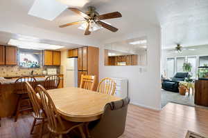 Dining area featuring a skylight, ceiling fan, a textured ceiling, light wood-type flooring, and baseboards