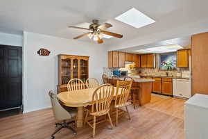 Dining space featuring a ceiling fan, a skylight, baseboards, and light wood finished floors