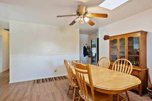 Dining room featuring a skylight, visible vents, a ceiling fan, light wood-type flooring, and baseboards