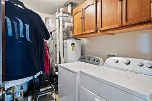 Laundry area featuring a textured ceiling, gas water heater, washing machine and clothes dryer, and cabinet space