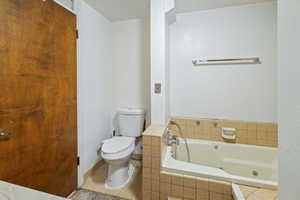 Bathroom with tile patterned floors, toilet, and tiled bath