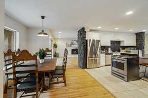 Kitchen with a stone fireplace, decorative light fixtures, appliances with stainless steel finishes, white cabinets, and backsplash