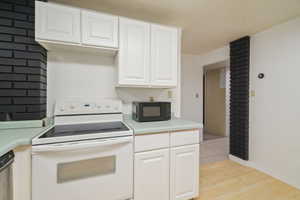 Kitchen with stainless steel dishwasher, white electric range oven, white cabinets, and light hardwood / wood-style floors