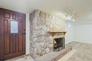 Foyer entrance with track lighting, a stone fireplace, and light carpet