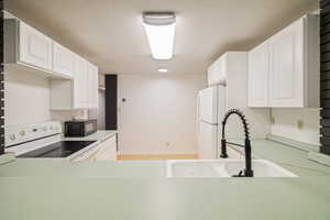 Kitchen featuring white cabinetry, sink, and white appliances