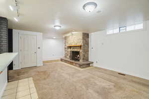 Unfurnished living room featuring track lighting, a stone fireplace, and carpet