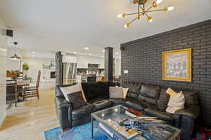 Living room with a notable chandelier, light hardwood / wood-style flooring, and brick wall