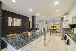 Kitchen with pendant lighting, a center island, white cabinets, light tile patterned flooring, and decorative backsplash