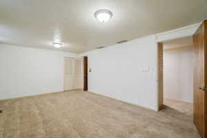 Basement featuring brick wall, light carpet, and a textured ceiling