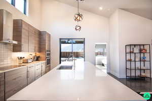 Kitchen with pendant lighting, sink, a towering ceiling, black electric stovetop, and wall chimney exhaust hood