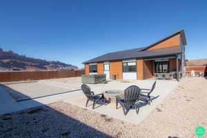 Back of house featuring a hot tub, a mountain view, a patio area, and a fire pit