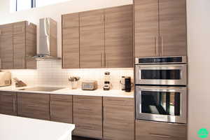 Kitchen featuring backsplash, stainless steel double oven, black electric stovetop, and wall chimney range hood