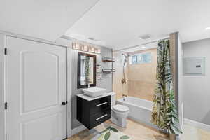 Full bathroom with electric panel, vanity, tile patterned floors, toilet, and shower / bath combo with shower curtain