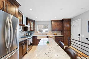 Kitchen featuring wall chimney exhaust hood, stainless steel appliances, sink, and light stone counters