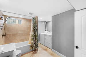 Bathroom with toilet, shower / bathtub combination with curtain, and separate washer and dryer