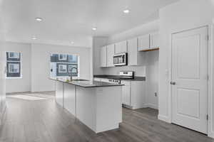 Kitchen with sink, a kitchen island with sink, stainless steel appliances, white cabinets, and light wood-type flooring