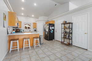 Kitchen featuring a breakfast bar area, vaulted ceiling, light tile patterned floors, kitchen peninsula, and stainless steel appliances